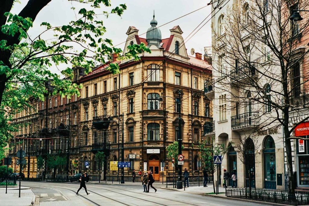 Street view of Krakow with historic architecture, tram tracks, and people walking under a canopy of spring trees.