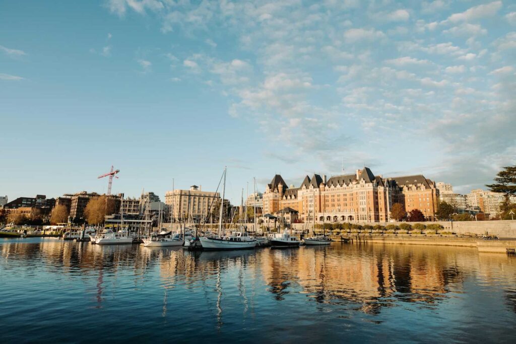 Victoria’s harbour with docked sailboats and historic buildings reflecting in the calm water during a golden hour sky